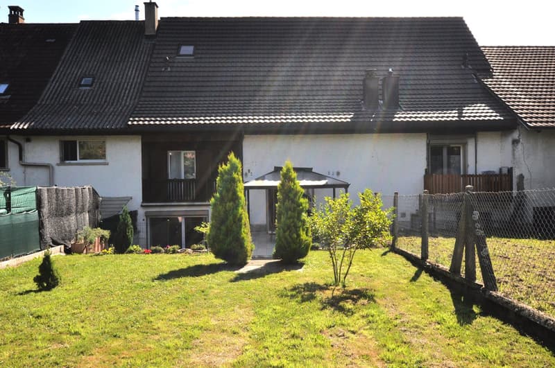 2-story house, tiled roof, white walls, windows with wooden frames, terrace on the second floor, fence, green lawn, shrubs, plants