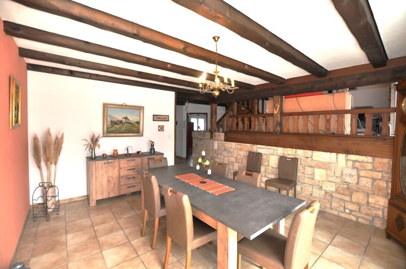 Dining room: wooden dining table, wooden cabinets, picture frame, chandelier, wall art, brick wall, tiled floor, wooden balcony railing, staircase