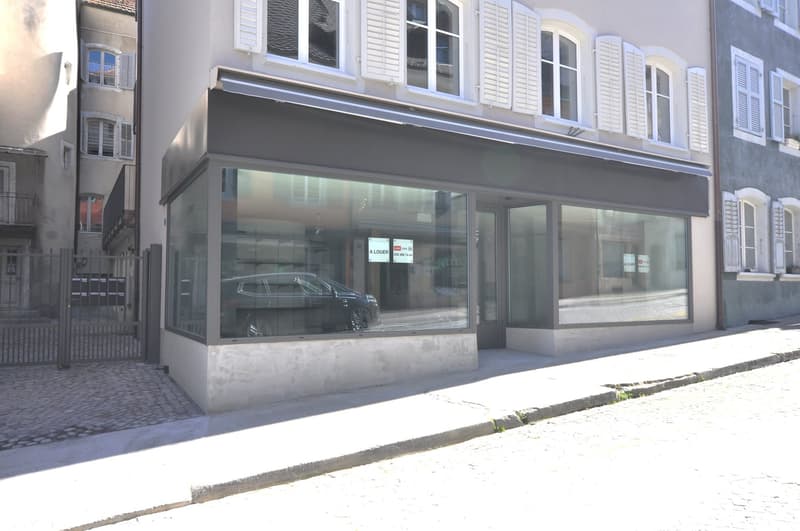 Facade of a building with glass windows and doors, metal gates, and a car parked in front