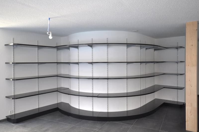 Curved shelving unit, white walls, black shelves, gray floor, power outlet