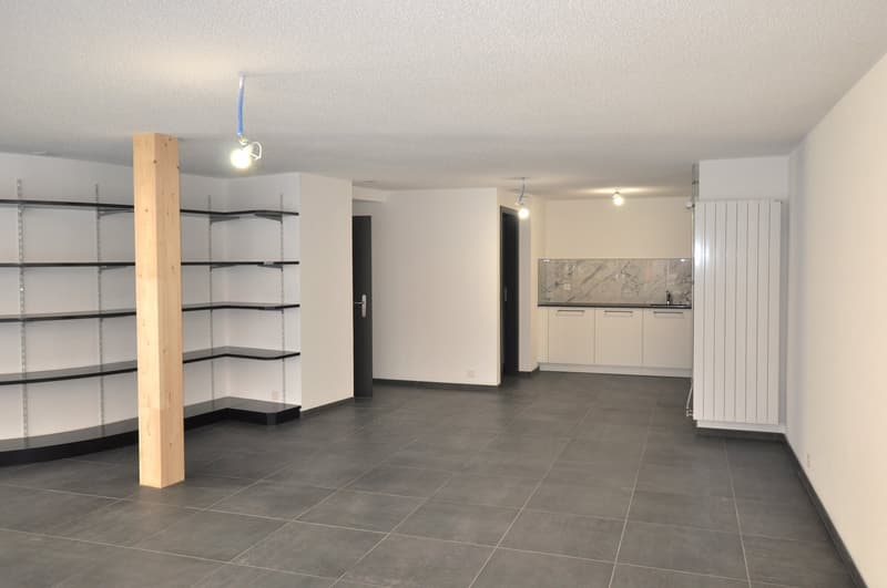 empty room, gray tile flooring, white walls, ceiling lights, wooden pillar, corner shelves, two doors leading to different rooms, counter with sink and cabinets