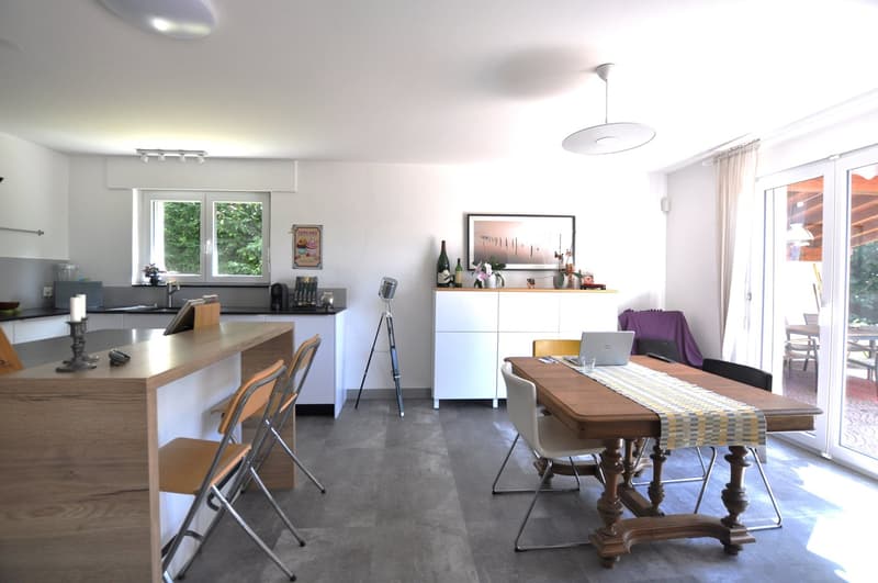 Kitchen: kitchen island, wooden floor, modern appliances, sink, faucet, windows, white cupboards, lamp. Dining room: wooden table, chairs, laptop, candle, wine bottles, picture frame, lamps.