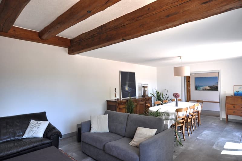 Living room with couches, dining table and chairs, and wooden beams.
