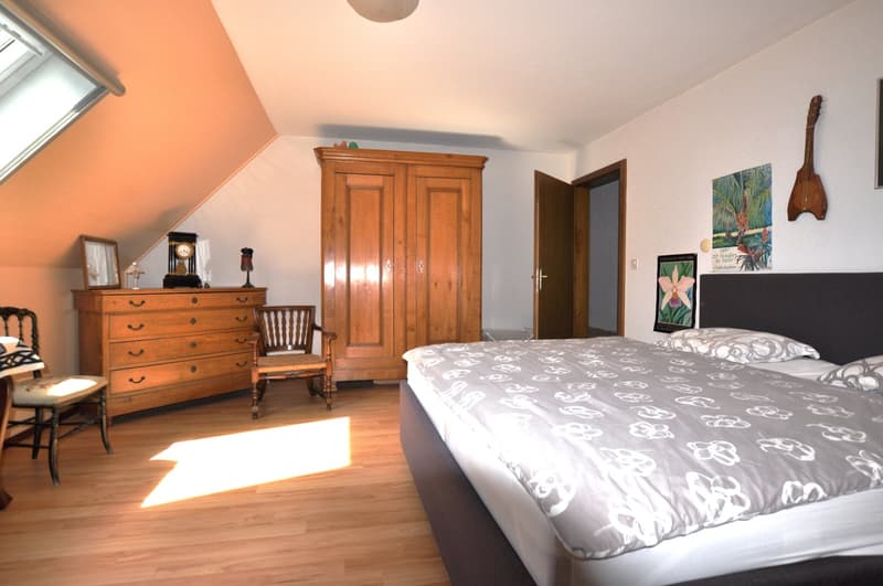 attic bedroom with wooden floor, large bed, wooden cabinet, chairs, decorative items, art on wall