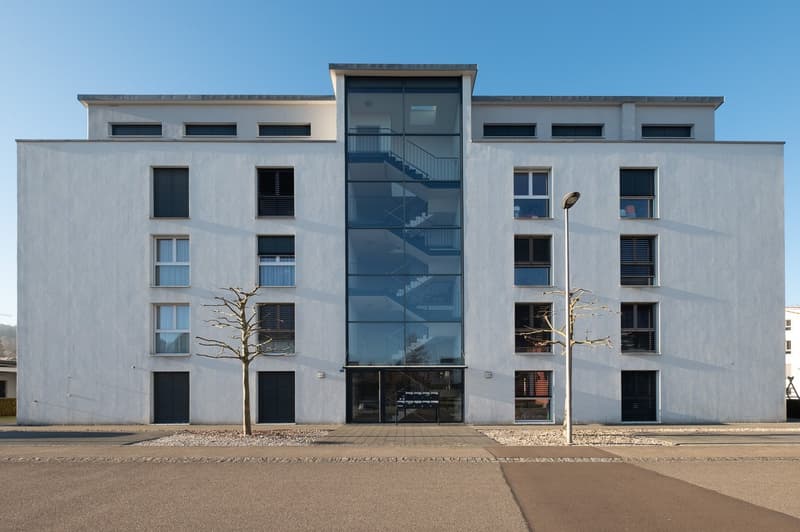 Contemporary design, white building, glass walls, multiple windows, staircases, entrance with sliding doors, paved sidewalk, street lighting.