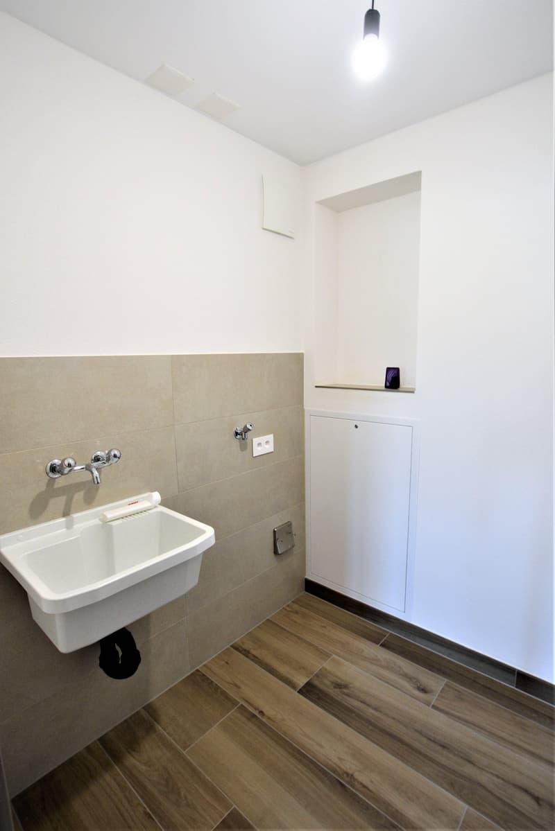 white sink, wooden floor, white walls, single electrical outlet, single switch