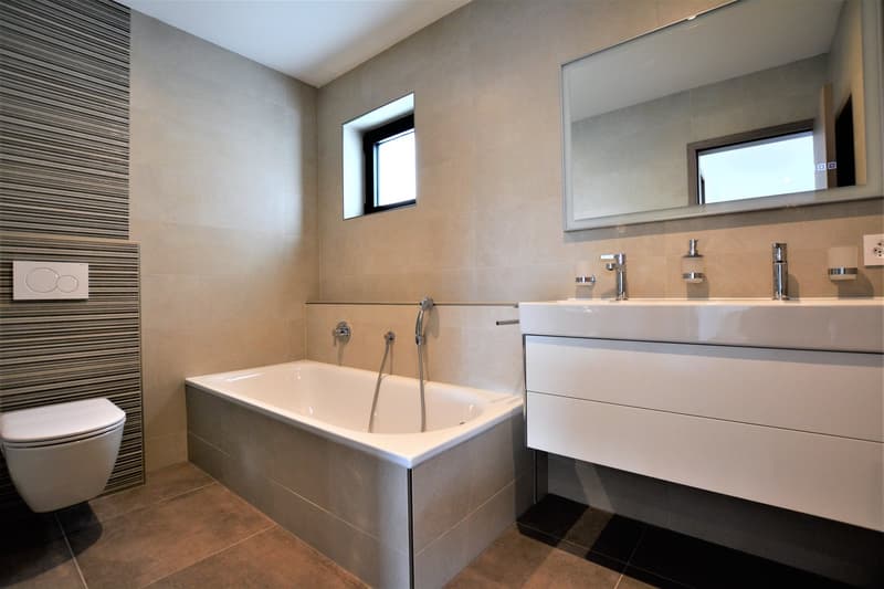 modern bathroom with bathtub, toilet, double sink, mirror, and built-in shelving