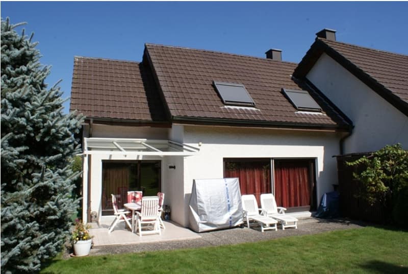 Single-family house, brown roof, white walls, patio, patio table and chairs, white chairs, brown wooden fence, green lawn, tree