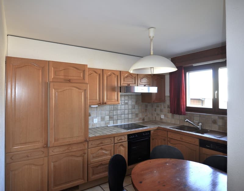 Kitchen with wooden cabinets, stove, sink, dishwasher, hanging lamp, window with curtain