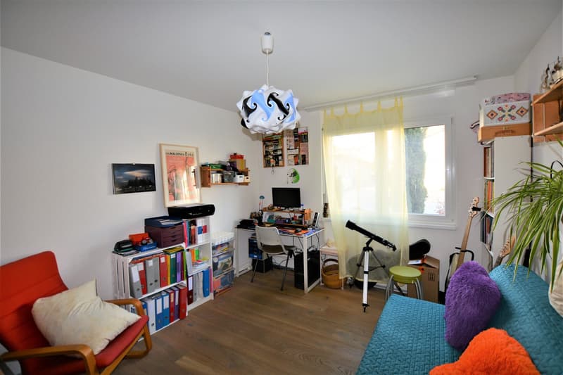 wooden floor, white walls, a red armchair, white desk with chair, a blue couch with two pillows, a telescope on a tripod