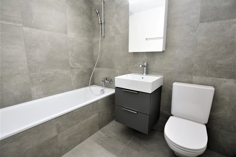 modern bathroom with bathtub, white sink and toilet, gray tiles, silver shower