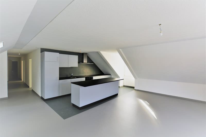 Empty room with white kitchen island, cabinets, counter top, ceiling light and sloping roof