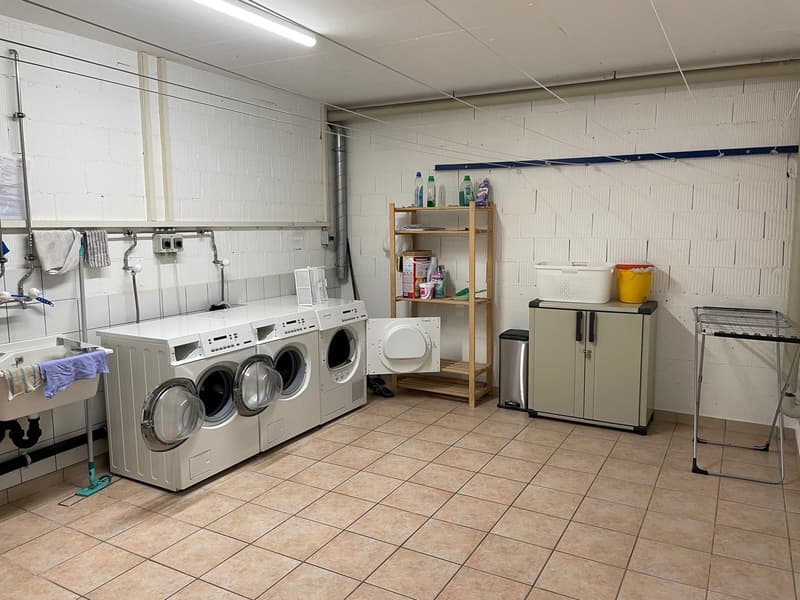 Four washing machines, two dryers, a wooden shelf, a trash bin, a drying rack