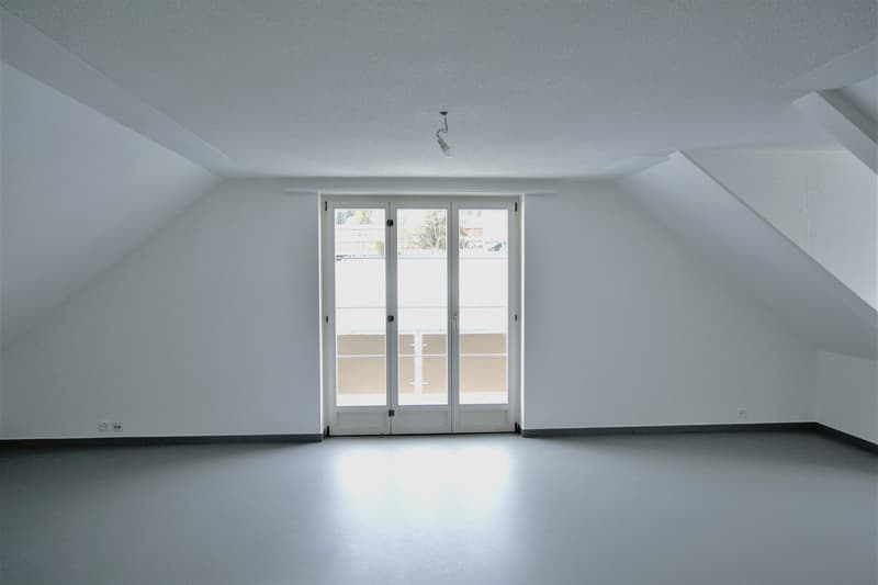 Empty room with white walls, gray floors, a double glass door, and a slanted ceiling.