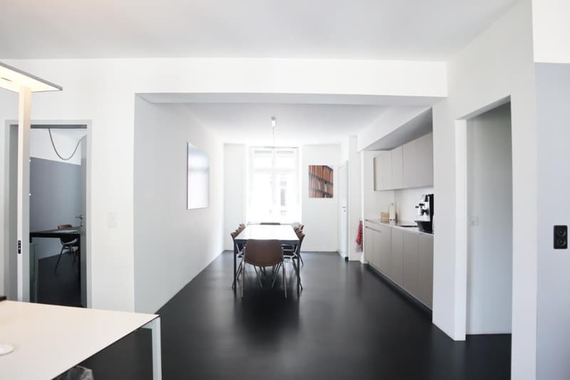 Modern open plan layout, white walls, black floors, large dining table, contemporary furniture, kitchen with appliances