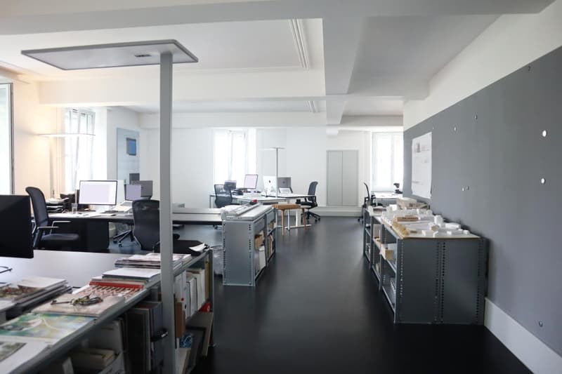 Empty office with desks, computers, chairs, lamps, bookshelves, gray walls, black floors