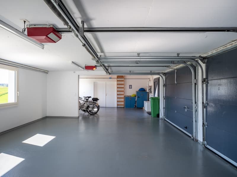 Empty garage with bicycles, ladder, cabinets, and trash bins.
