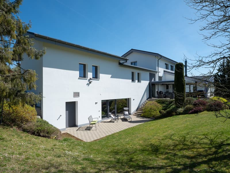 Modern white house with a flat roof, large windows, and a patio with outdoor furniture.
