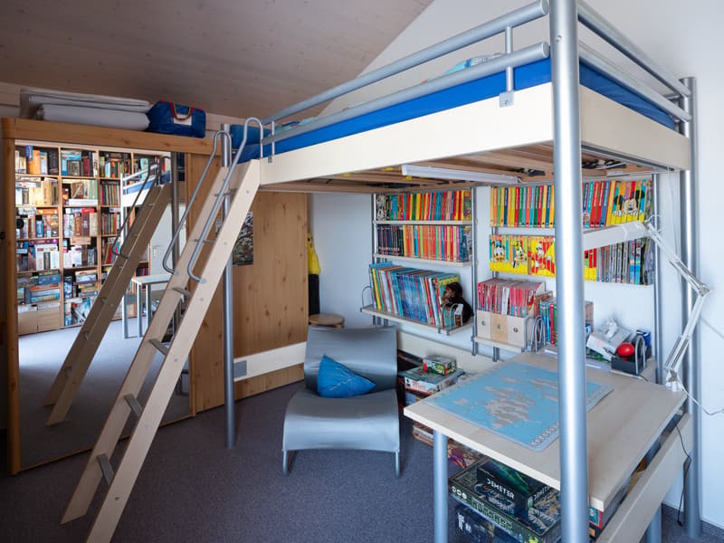 A room with a bunk bed, ladder, chair, desk, bookshelves, books, pillow, map, toys, lamp, and mirror.