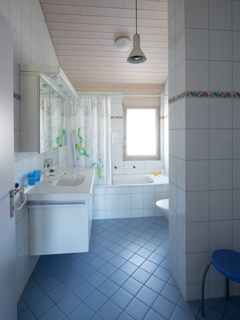 Bathroom with white tiles, blue floor, white sink, mirror, bathtub, and shower curtain. A lamp is hanging from the ceiling.