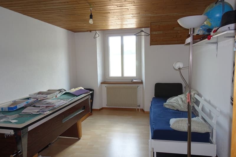 room with table and bed, wooden floor, wooden ceiling, window, radiator
