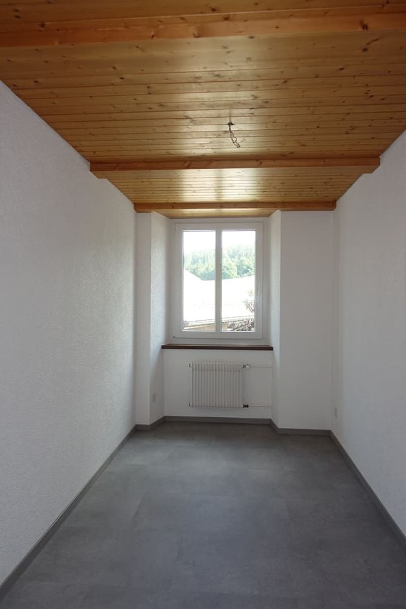 empty room, white walls, wooden ceiling, gray floor, window with white radiator
