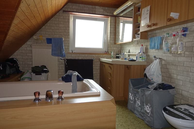 small bathroom with tub, sink, and toilet, radiator, wooden cabinet, shelves, window, towels, and storage bags