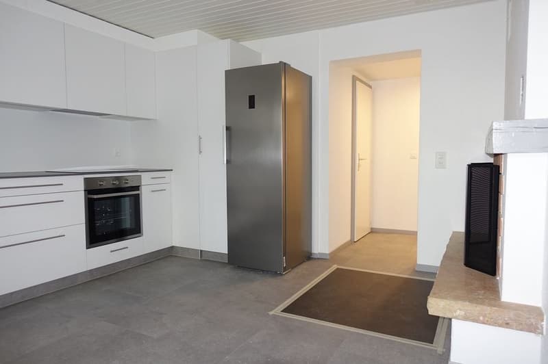 Empty modern kitchen with integrated appliances, stone floor, white cabinetry, fireplace in adjacent room