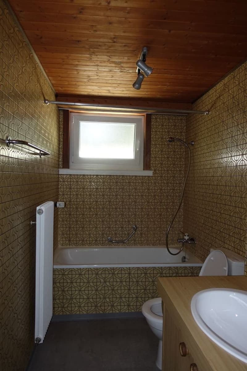 tiled walls and floor, bathtub with faucet and showerhead, white toilet, sink, wooden cabinet, radiator