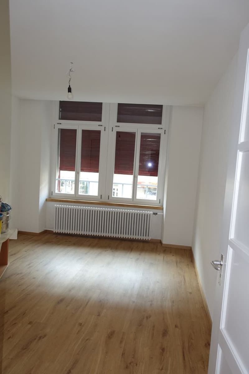 wooden floor, white walls, 2 windows with brown wooden blinds, balcony, radiator, view of building