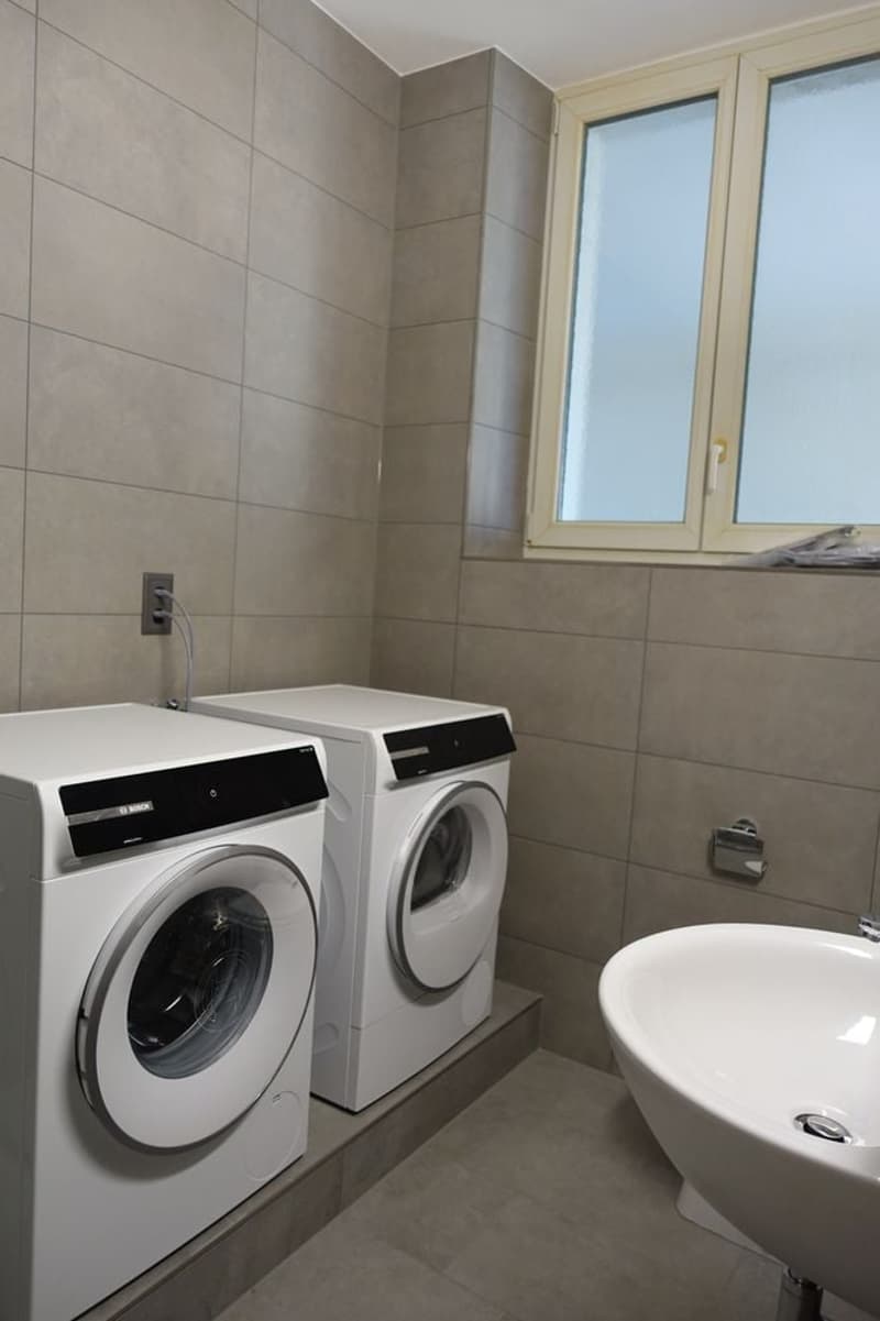 A laundry room with tiled floor and walls, including a white washing machine, dryer, and a sink.