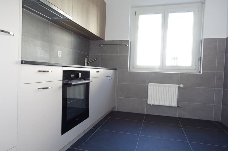 gray tile wall, blue tile floor, white cabinet, electric stove, window, radiator