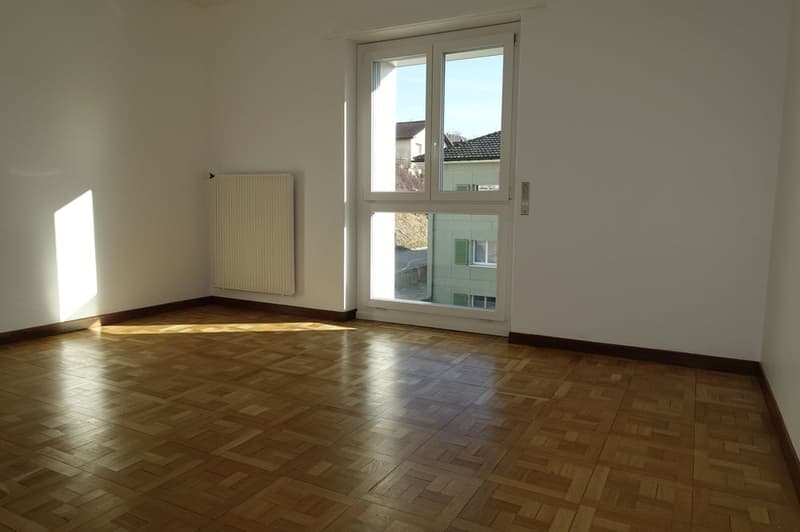 Empty room with wooden floors, large windows, white walls, and a white radiator.