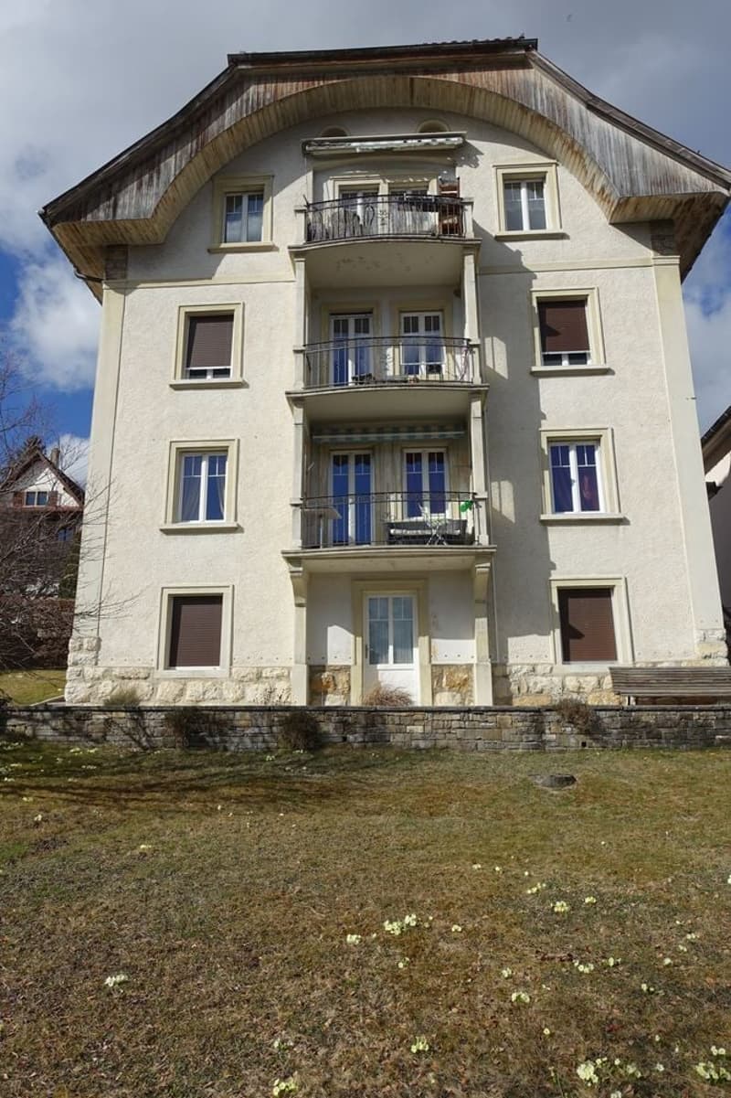 2 story house, large balcony, multiple windows, stone wall, grassy yard