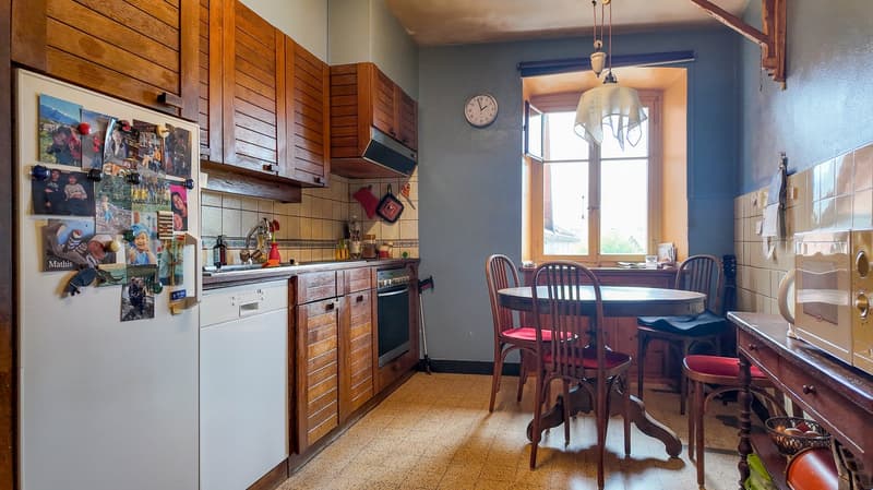 Wooden cabinets, white refrigerator, tiled floor, dining table and chairs, microwave, clock, and large window