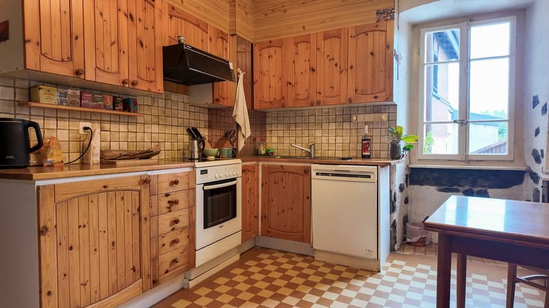 Wooden cabinets, tiled backsplash, kitchen appliances, checkered floor, window, wooden table, dishwasher, washing machine.
