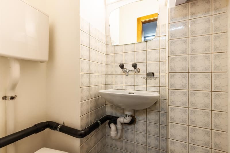 tiled walls, white sink, wall-mounted faucet, mirror, and white toilet