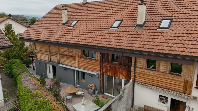 two-story house, brown roof, wooden exterior, several windows, wooden balcony, and garden area