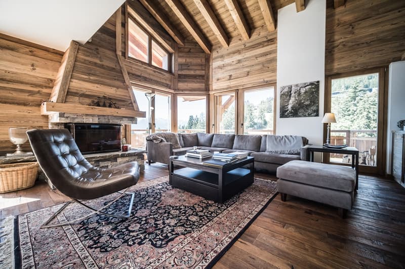 wooden floor, wooden walls, fireplace, two sofas, coffee table, armchair, ottoman, large glass windows, decor items