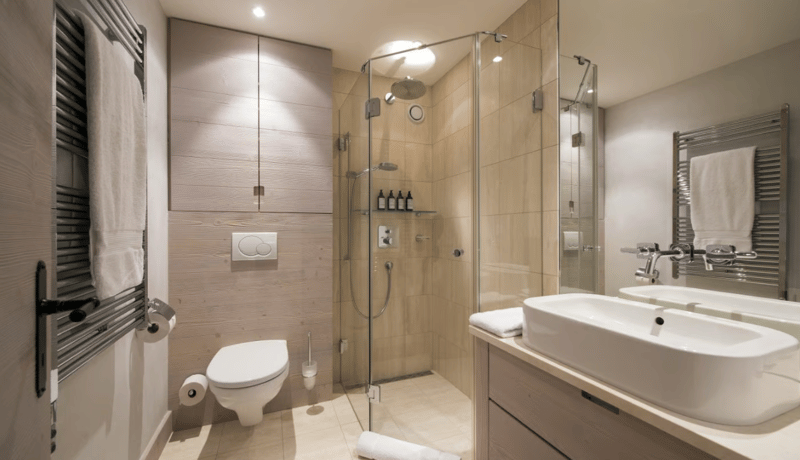 modern bathroom with walk-in shower, white toilet, double sink, wooden cabinets, wall mounted towel racks, tiled floor