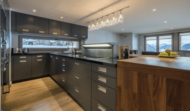 modern kitchen, wooden flooring, granite countertop, stainless steel appliances, large windows, chandelier, dishwasher, sink with faucet, kitchen island, wine bottle