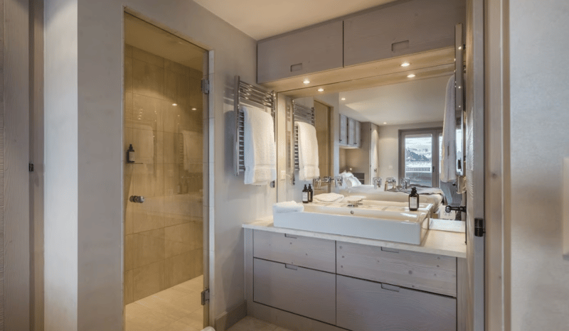 White sink, large mirror, large shower, white towels, wooden cabinets, and toiletries.