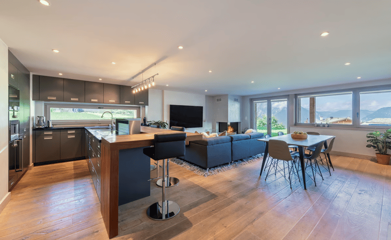 Wooden floor, white walls, large windows, fireplace, kitchen island, dining table, living room couch, television, bar stools