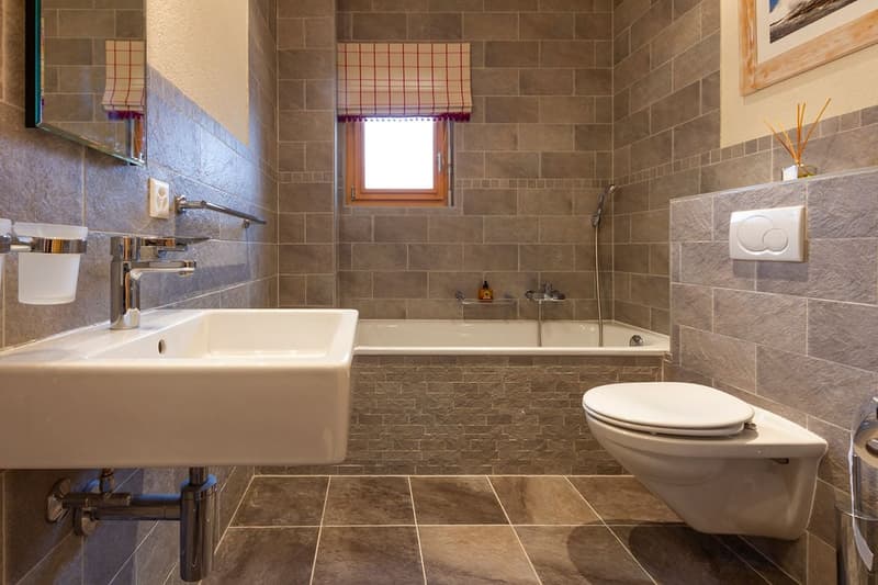 Large bathroom with tiled walls, a bathtub, a sink, and a toilet. The bathroom has a window and appears to be well-lit.