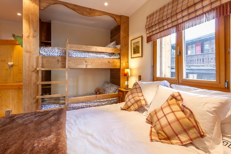 Rustic wooden bunk beds, plaid and patterned bedding, wooden walls and furniture, large window with roman shade