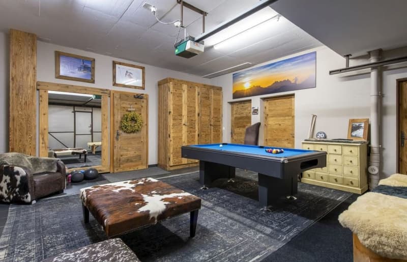 Spacious game room with a pool table, leather couch, wooden cabinets, and large artwork on the walls. The room has a rustic, mountain-inspired decor with a fireplace and other amenities.