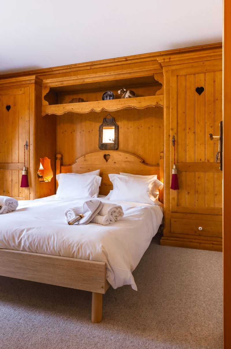 double bed with white pillows and comforters, wooden bedside table, wardrobe, and mirror, wooden walls, carpeted floor