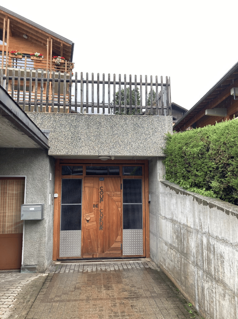 raised ground floor entrance with wooden doors, entrance on sidewalk, railing above, box for mail and light fixture