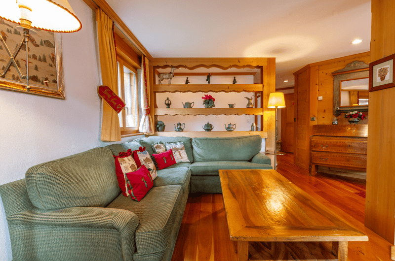 Wooden floor, cream walls, wooden shelf, floor lamp, sectional sofa with decorative pillows, coffee table, cabinet with drawers
