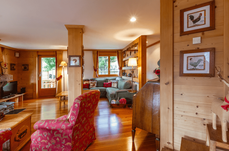 wooden walls, hardwood floor, sofa, armchair, lamp, window, TV stand with television, shelves with picture frames, fireplace